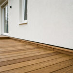 Terrasse en bois propre et bien drainée le long d’une façade claire, protégée de l’humidité hivernale.