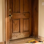 Remplacement soigneux d’une ancienne porte d’entrée par une nouvelle porte en bois parfaitement alignée, avec des outils de mesure disposés à proximité.